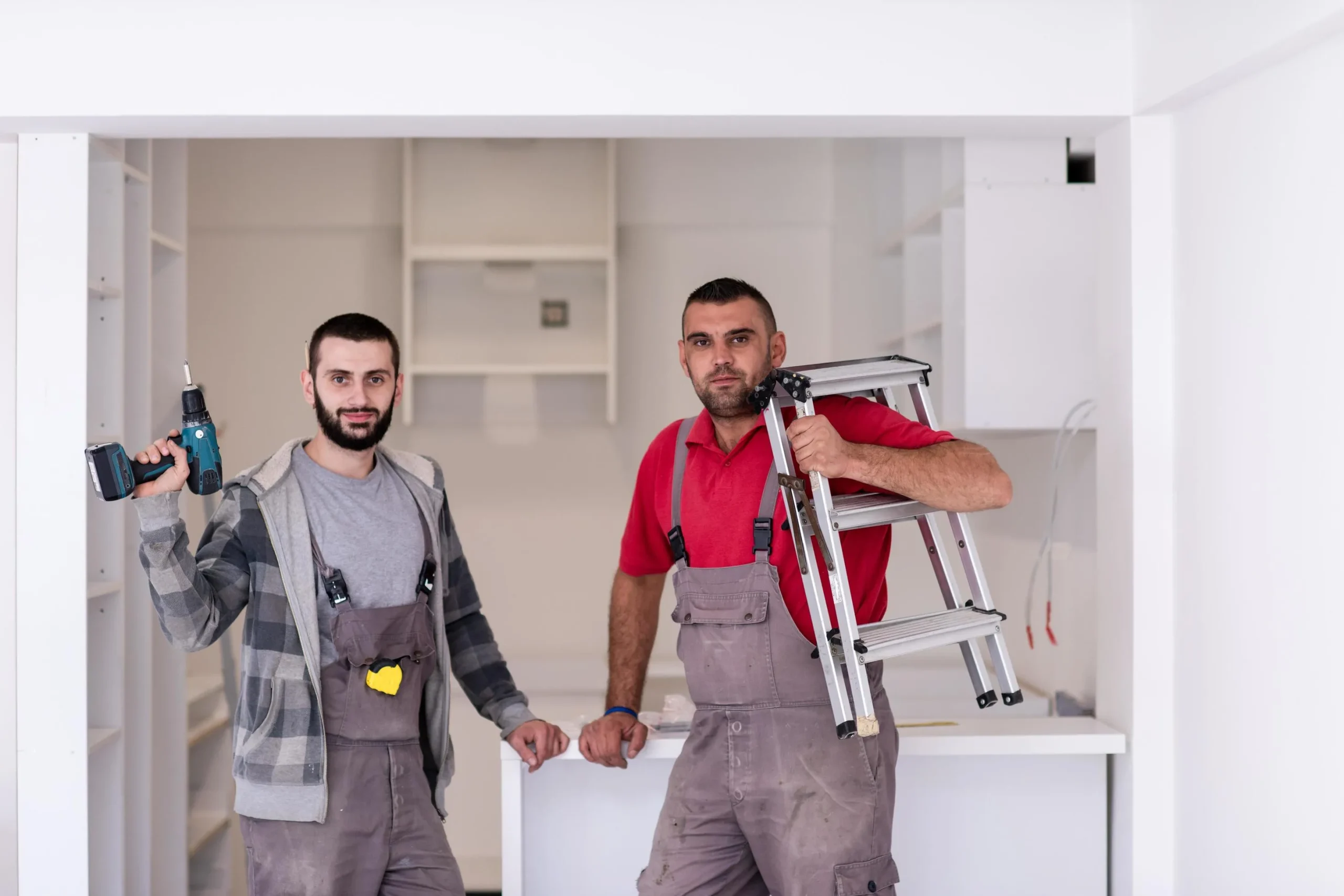 Two contractors posing with a power drill and a stepladder in a kitchen under renovation.